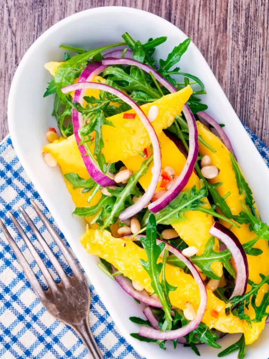 Overhead spicy mango salad with chilli, red onion, rocket (arugula), lime and pine nuts.