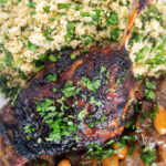 Close up overhead tamarind and honey glazed duck leg with stewed onions and couscous.