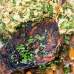 Close up overhead tamarind and honey glazed duck leg with stewed onions and couscous.