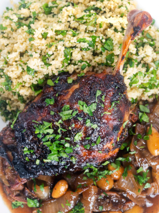 Close up overhead tamarind and honey glazed duck leg with stewed onions and couscous.