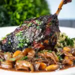 Close up tamarind and honey glazed duck leg with stewed onions, dates and almonds.