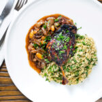 Overhead tamarind and honey glazed duck leg with stewed onions and couscous.