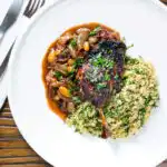 Overhead tamarind and honey glazed duck leg with stewed onions and couscous.