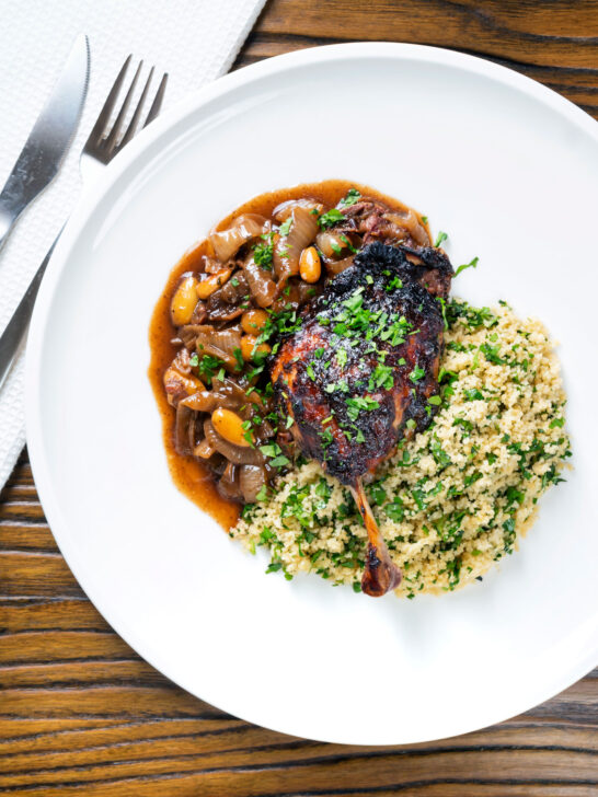 Overhead tamarind and honey glazed duck leg with stewed onions and couscous.