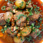 Overhead close-up spicy Thai beef massaman curry with potatoes, shallots and peanuts featuring a title overlay.