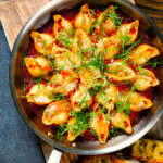 Overhead skillet baked stuffed pasta shells with goat's cheese and nduja in a tomato sauce.