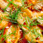 Overhead close-up baked stuffed pasta shells with goat's cheese and nduja in a tomato sauce.