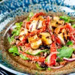 Close-up grilled and marinated halloumi salad with peppers, couscous and chickpeas featuring a title overlay.