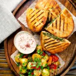 Overhead minced lamb arayes stuffed pita breads served with batata harra and yoghurt dip.