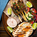 Overhead lamb kofta kebabs with pitas, salad and pomegranate yoghurt dip.