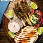 Overhead lamb kofta kebabs with pitas, salad and pomegranate yoghurt dip featuring a title overlay.