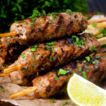Minced lamb kofta kebab skewers with a lime wedge.