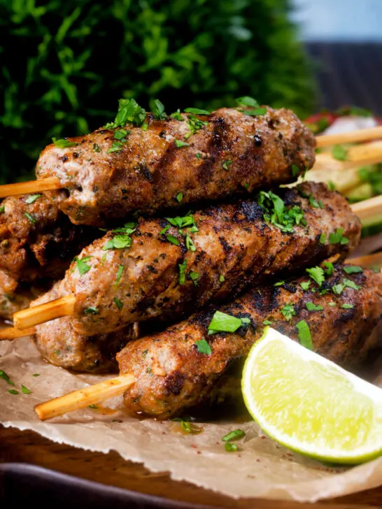 Minced lamb kofta kebab skewers with a lime wedge.