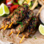 Minced lamb kofta kebab skewers with lime wedges and salad.