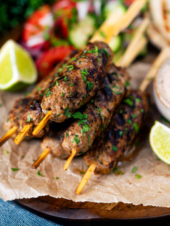 Minced lamb kofta kebab skewers with lime wedges and salad.