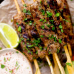 Overhead close up minced lamb kofta kebab skewers a yoghurt dip.