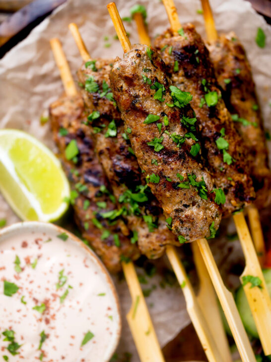 Overhead close up minced lamb kofta kebab skewers a yoghurt dip.