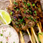 Overhead close up minced lamb kofta kebab skewers a yoghurt dip featuring a title overlay.