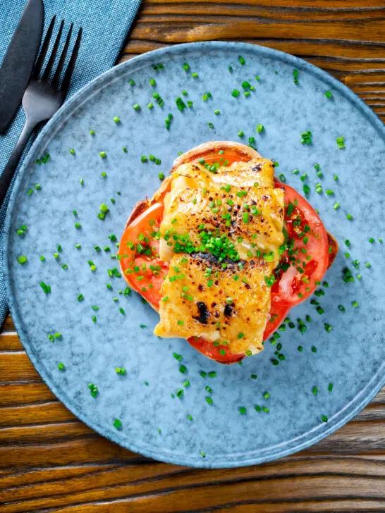 Overhead smoked haddock rarebit on toast with tomatoes garnished with chives.