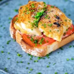 Smoked haddock rarebit on toast with tomatoes garnished with chives.