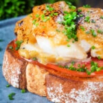 Close-up smoked haddock rarebit on toast with tomatoes garnished with chives.