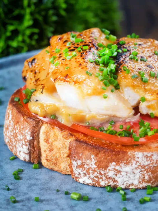 Close-up smoked haddock rarebit on toast with tomatoes garnished with chives.