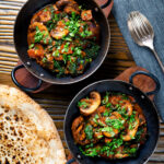 Overhead vegan spinach and mushroom Indian inspired curry served with naan bread.