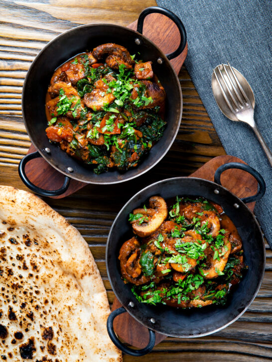 Overhead vegan spinach and mushroom Indian inspired curry served with naan bread.