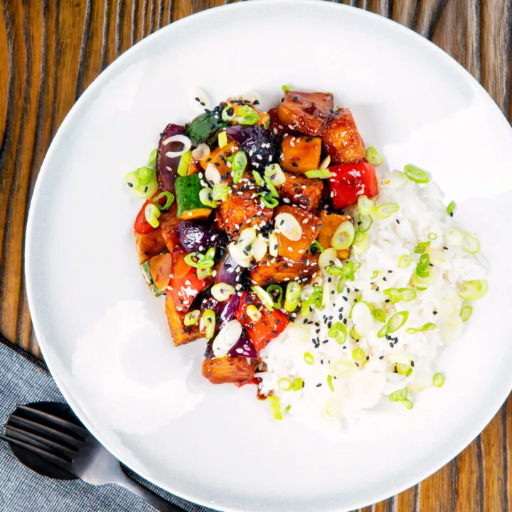 Vegan sweet and sour tofu with vegetables and pineapple served with steamed rice and green onions.