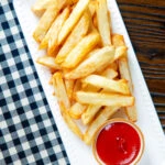 Overhead air fryer golden crispy British chips served with a bowl of ketchup.