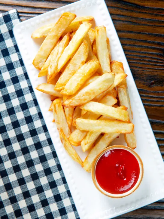 Overhead air fryer golden crispy British chips served with a bowl of ketchup.