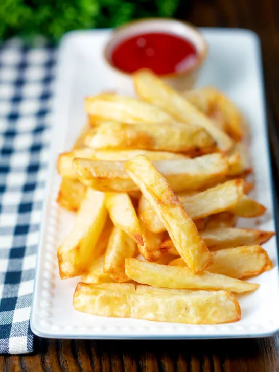 Air fryer golden crispy British chips served with a bowl of ketchup.