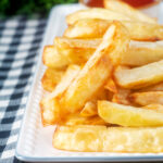Close-up air fryer golden crispy British chips served with a bowl of ketchup.