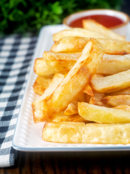 Close-up air fryer golden crispy British chips served with a bowl of ketchup.