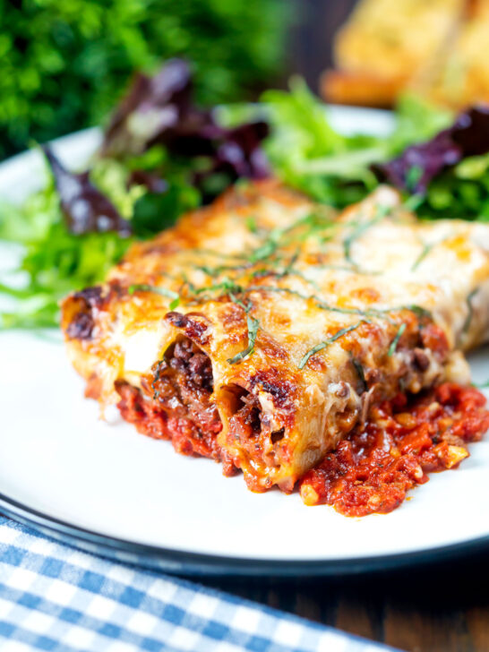 Minced beef stuffed cannelloni with bechamel and mozzarella cheese served on a plate.