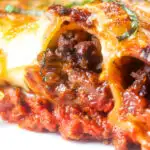 Close-up beef stuffed cannelloni with bechamel and mozzarella cheese served on a plate featuring a title overlay.