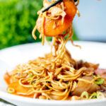 British Chinese takeaway style chicken chow mein noodles being picked up with chopsticks.