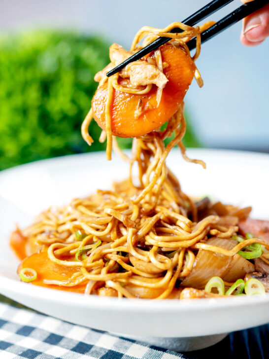 British Chinese takeaway style chicken chow mein noodles being picked up with chopsticks.