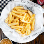 Overhead chip shop style chippy chips served with a side of curry sauce.