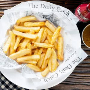 Proper chip shop style chippy chips served in "newspaper" with curry sauce on the side.
