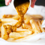 Homemade British chippy curry sauce being poured over chip shop chips.