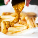 Homemade British chippy curry sauce being poured over chip shop chips.