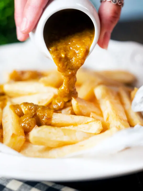 Homemade British chippy curry sauce being poured over chip shop chips.