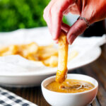 Homemade British chip shop style chips being dipped into chippy curry sauce.