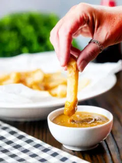 Homemade British chip shop style chips being dipped into chippy curry sauce.