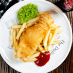 Overhead chip shop style fried battered fish served with chips and mushy peas.