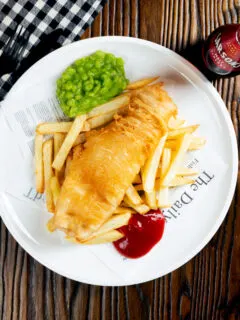 Overhead chip shop style fried battered fish served with chips and mushy peas.