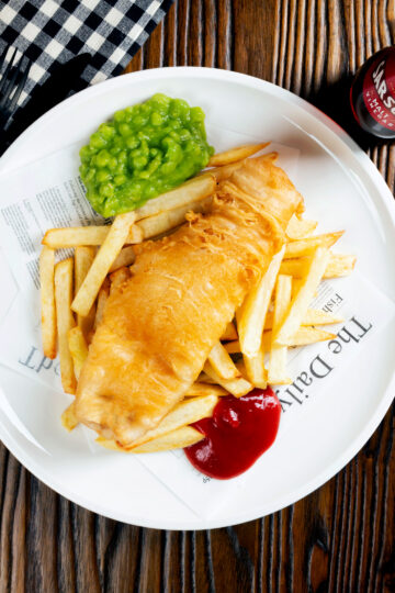 Overhead chip shop style fried battered fish served with chips and mushy peas.