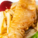 Close-up chip shop style fried battered fish served with chips and mushy peas.
