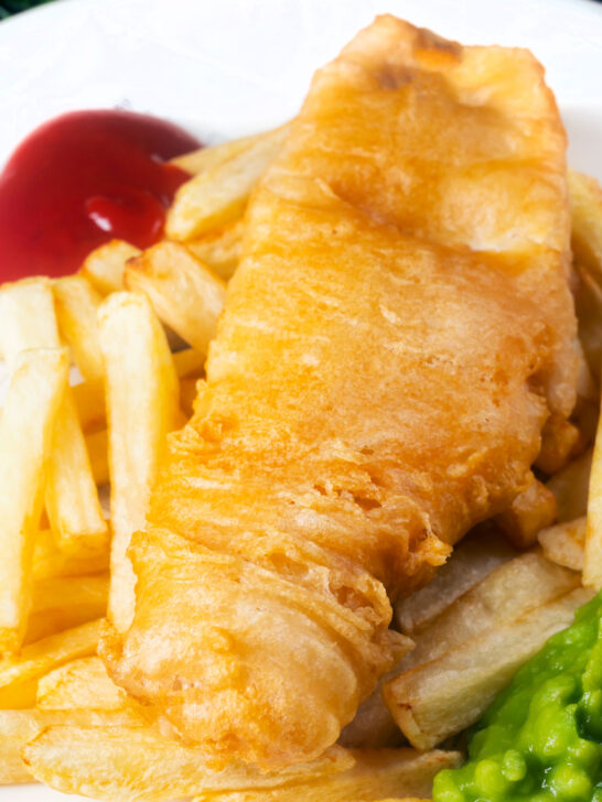 Close-up chip shop style fried battered fish served with chips and mushy peas.